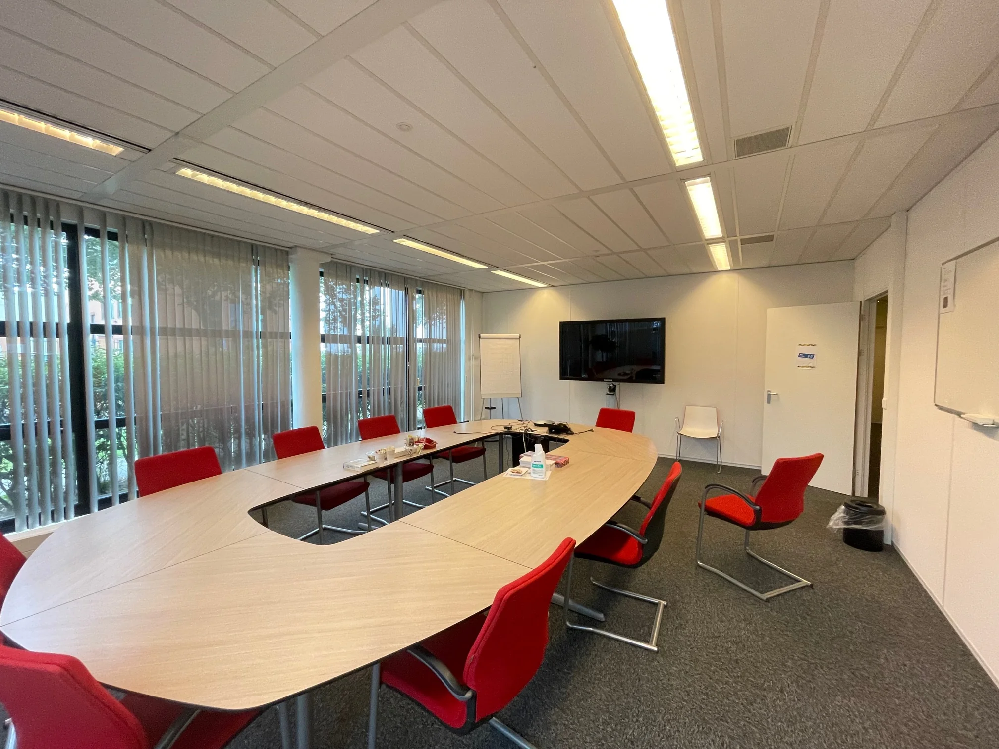 Vergaderruimte aan de Karel Doormanweg met ovale tafel, rode stoelen, presentatiescherm en flipover.